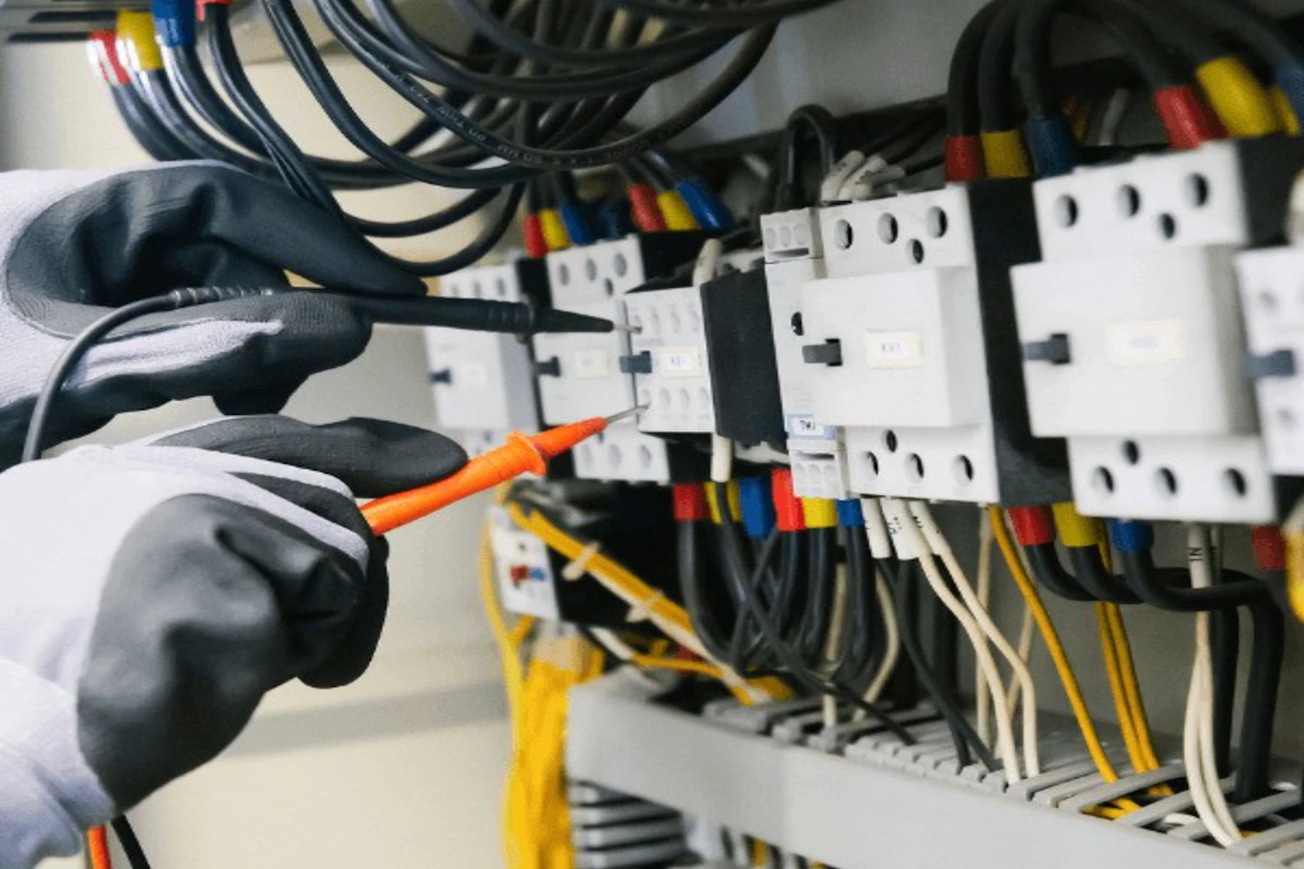 Technician testing wiring inside an electrical control panel during installation