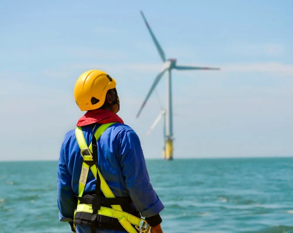 Engineer in a hard hat and safety gear looking up at a wind turbine